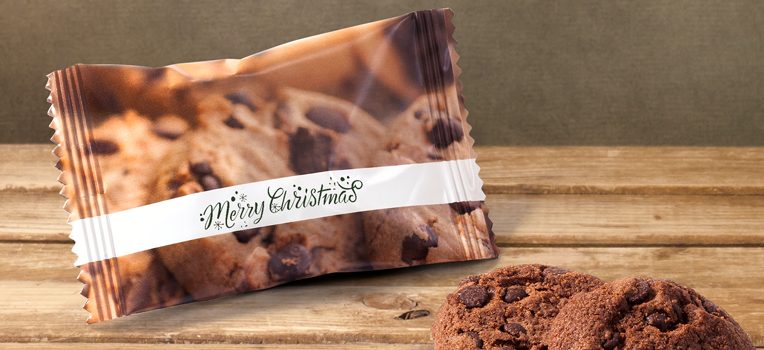 En chokladkaka i festlig förpackning märkt God Jul sitter på en träyta bredvid två oinslagna chokladkakor.